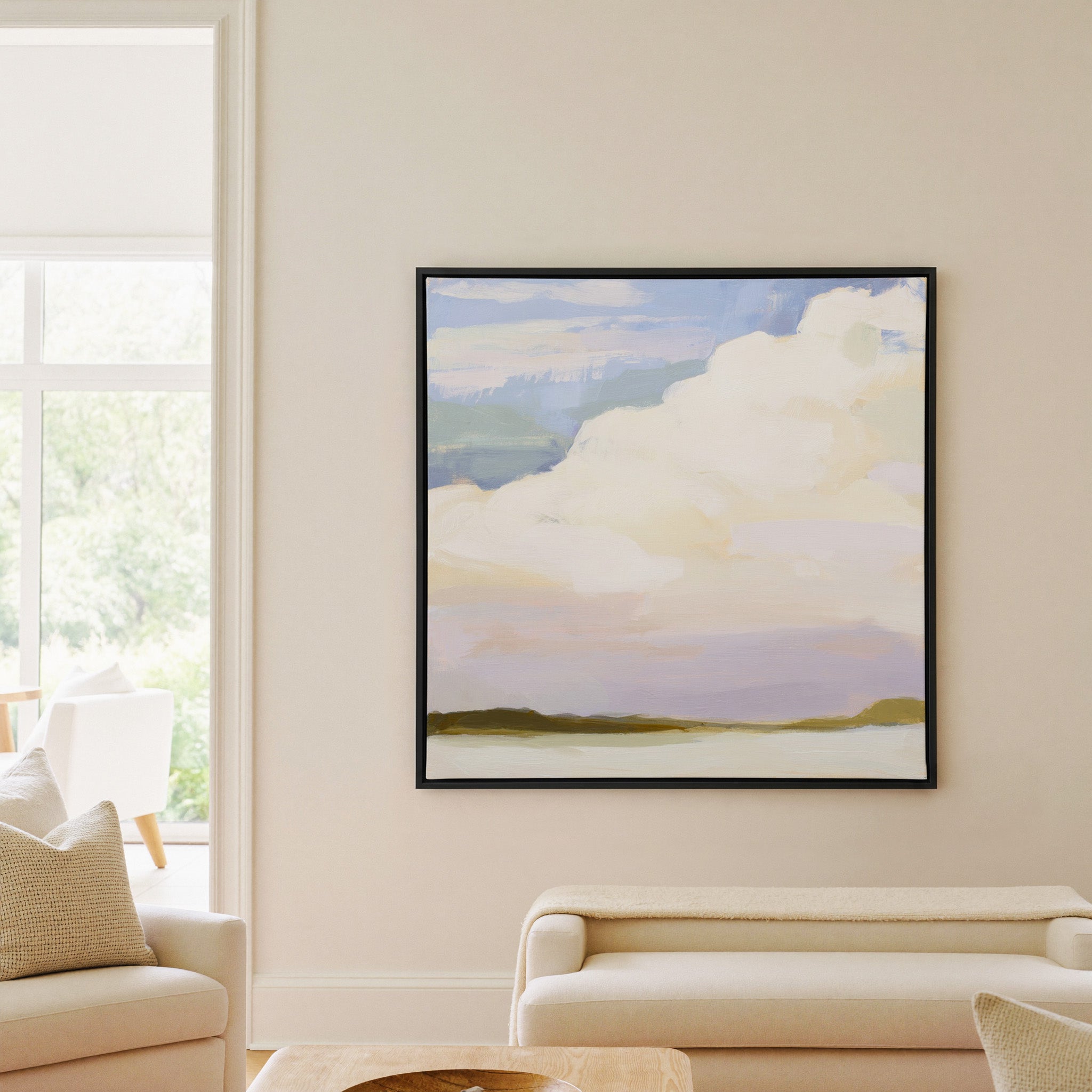 soft white clouds over pale blue and lavender canvas wall art in a black frame in a living room