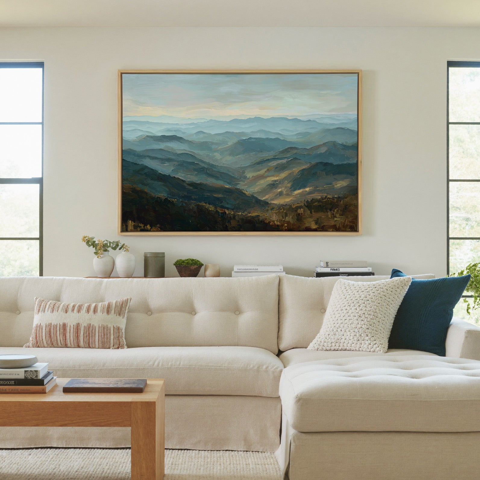 layered blue ridgelines with pale sky and warm canvas wall art in a natural wood frame in a living room