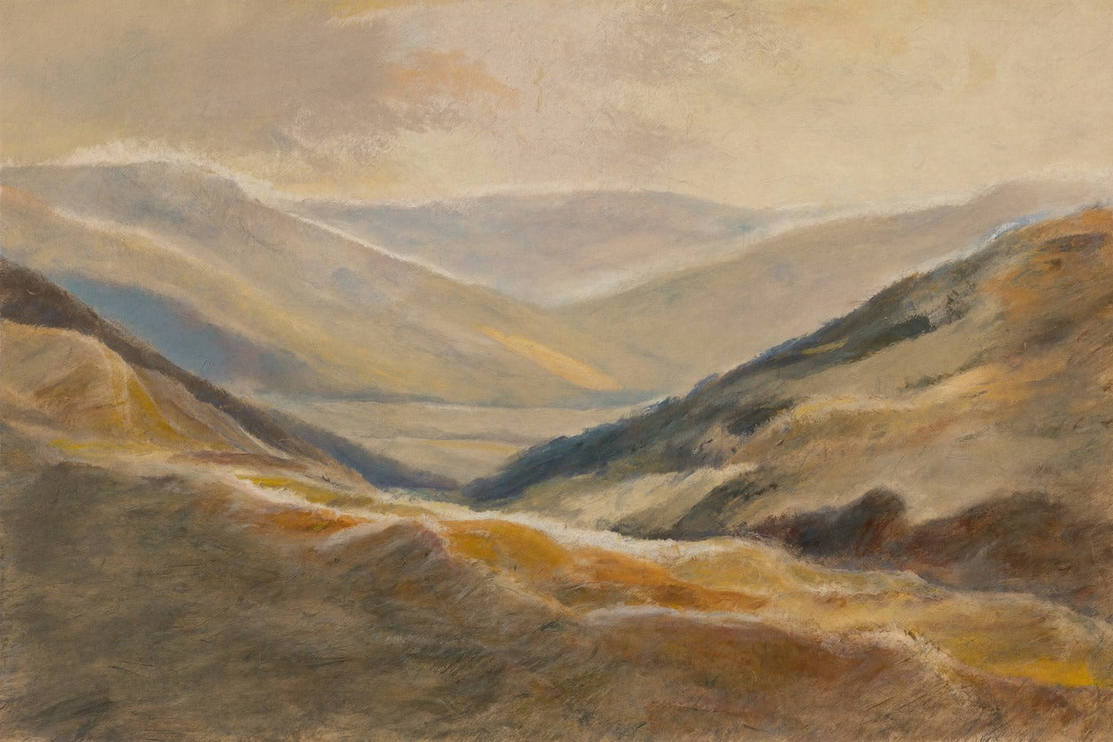 Beige and blue-gray mountain ridges opening to a pale valley under a hazy sky