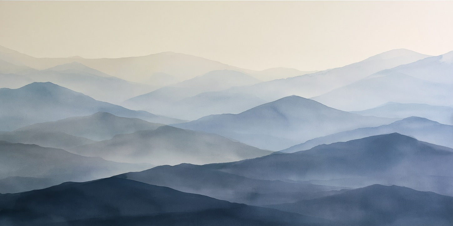 Layered blue mountain ridges fading into mist under a pale sky, with soft blue mountain layers