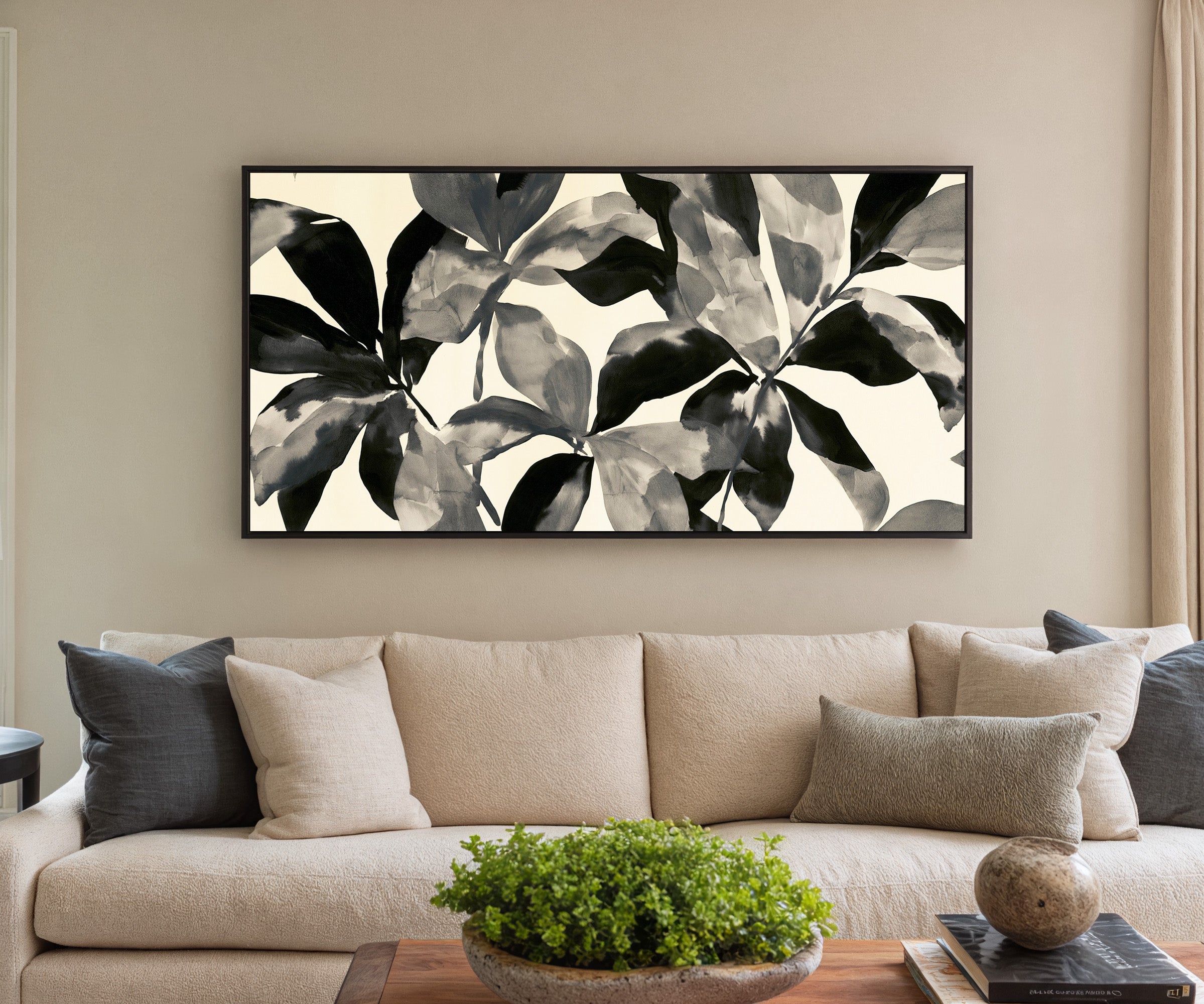 overlapping black and gray leaf shapes on cream canvas wall art in a black frame in a styled room setting
