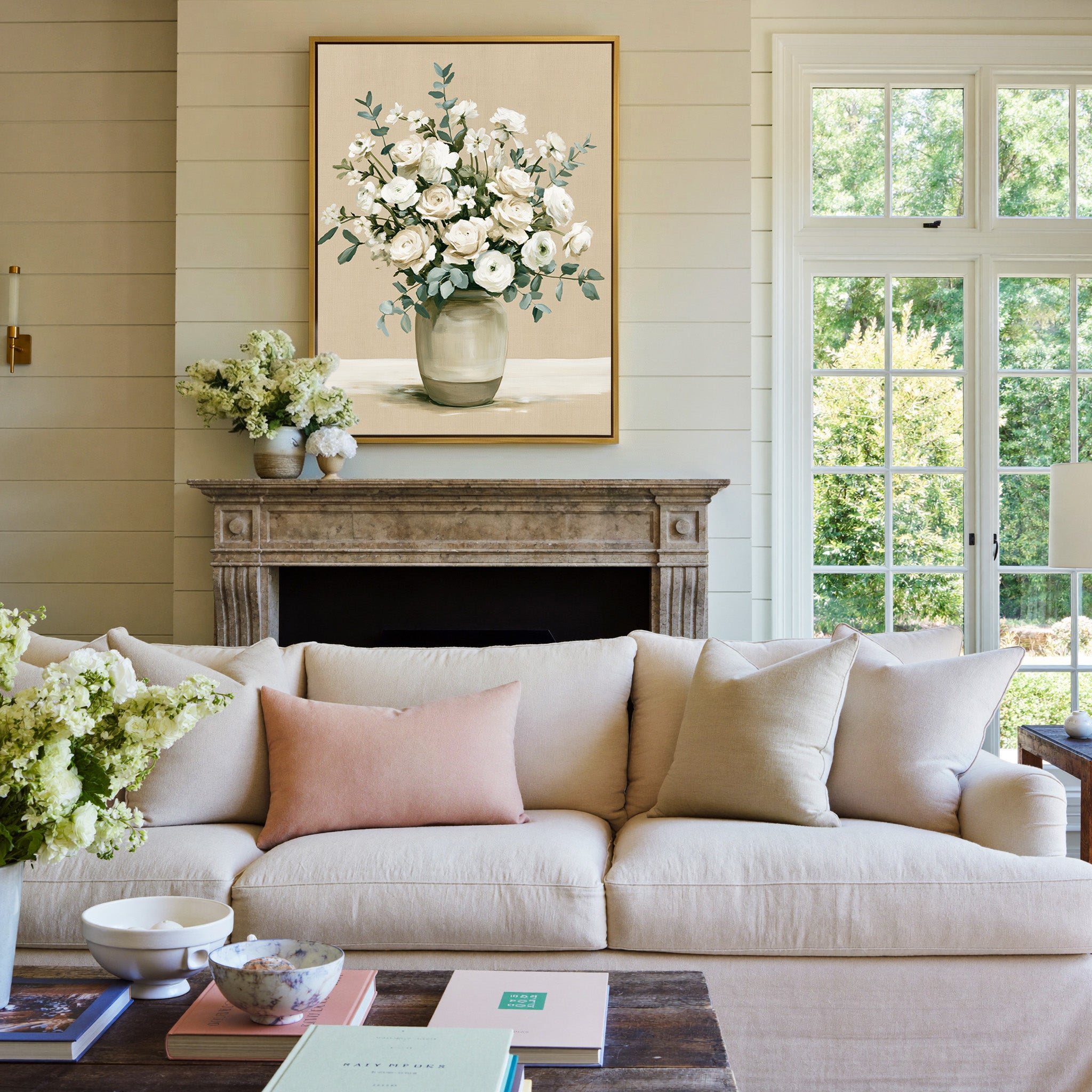 white roses and ranunculus in a glass vase canvas wall art in a gold frame above a mantel