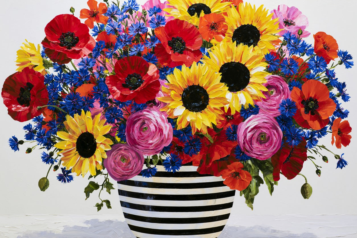 Dense bouquet of red poppies, yellow sunflowers, and blue cornflowers in a striped vase
