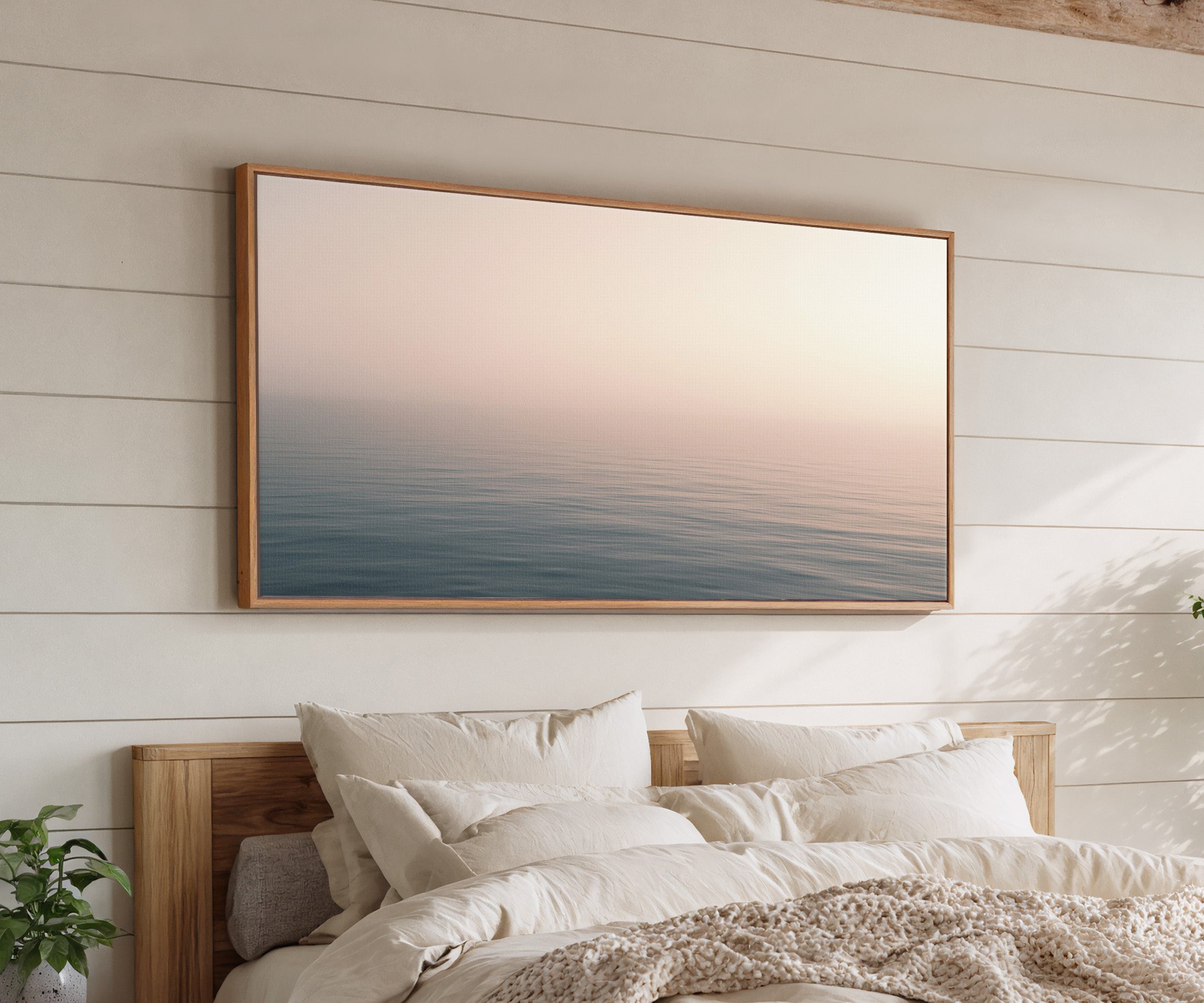 soft blush and blue seascape canvas wall art in an oak frame above a bed