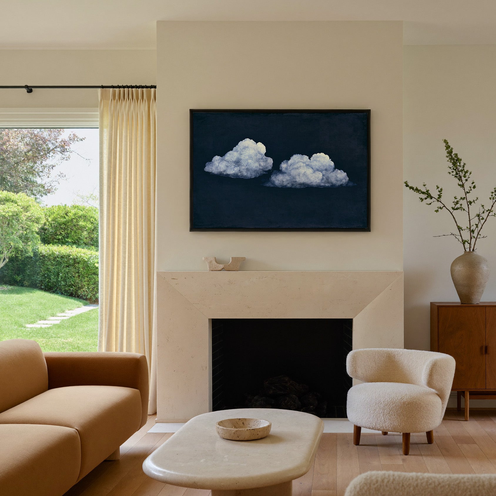 two pale clouds on a deep navy field canvas wall art in a black frame above a mantel