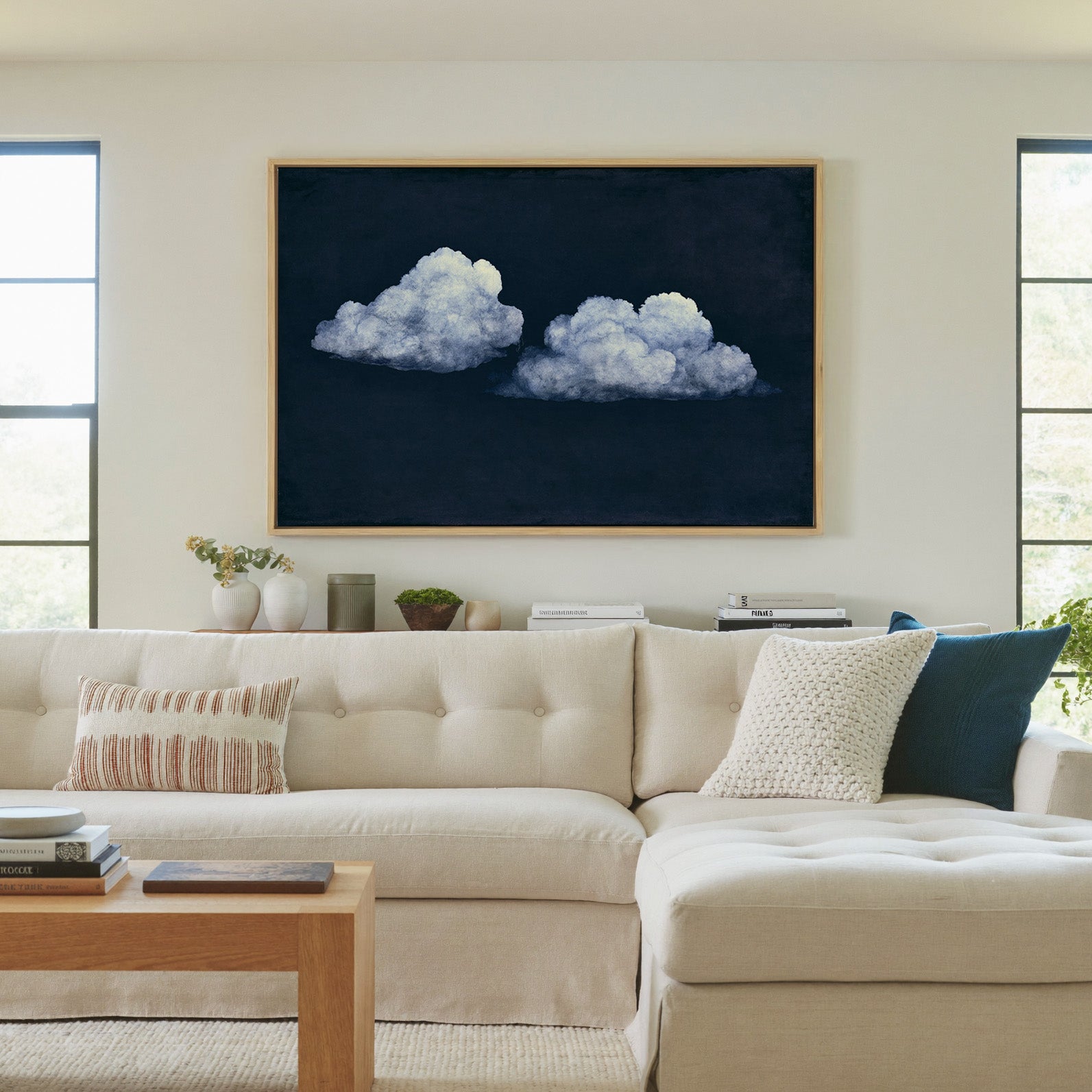 two pale clouds on a deep navy field canvas wall art in a natural wood frame in a living room