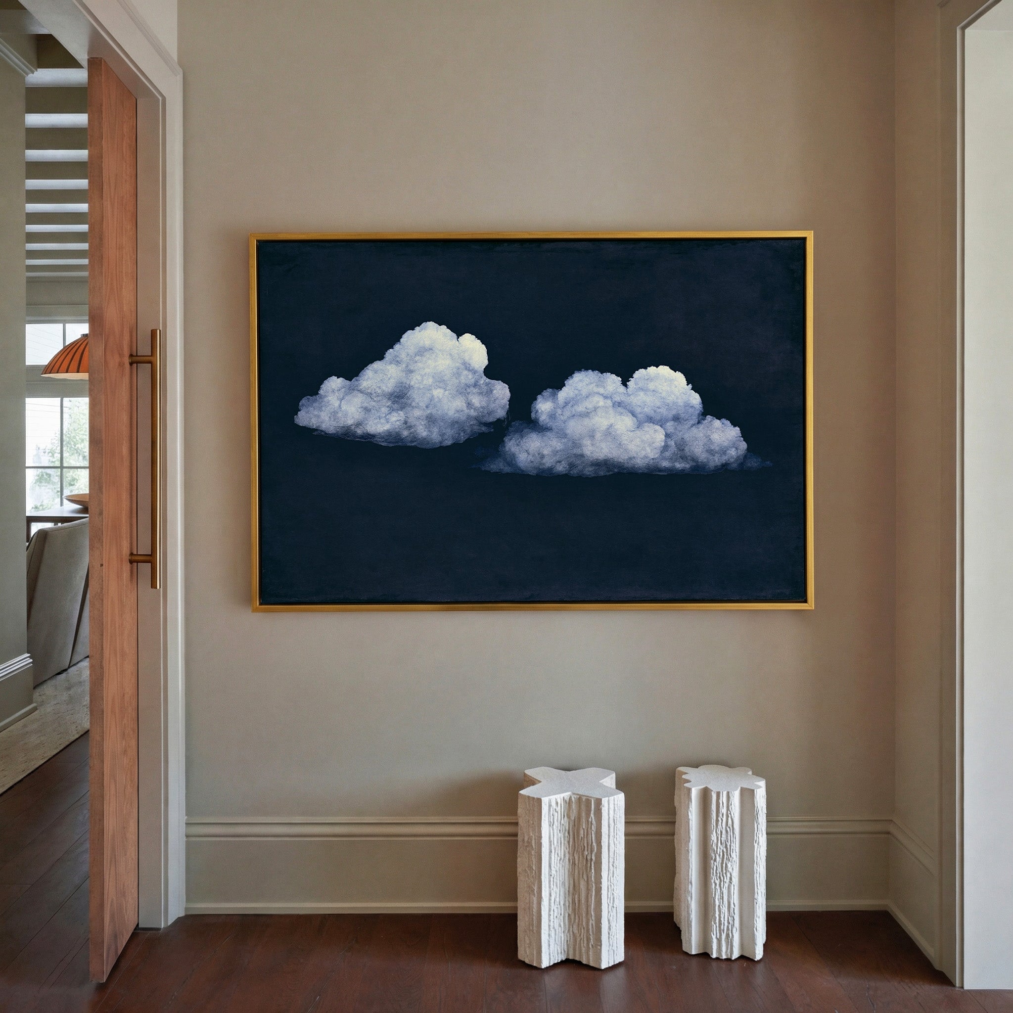 two pale clouds on a deep navy field canvas wall art in a gold frame in a styled room setting