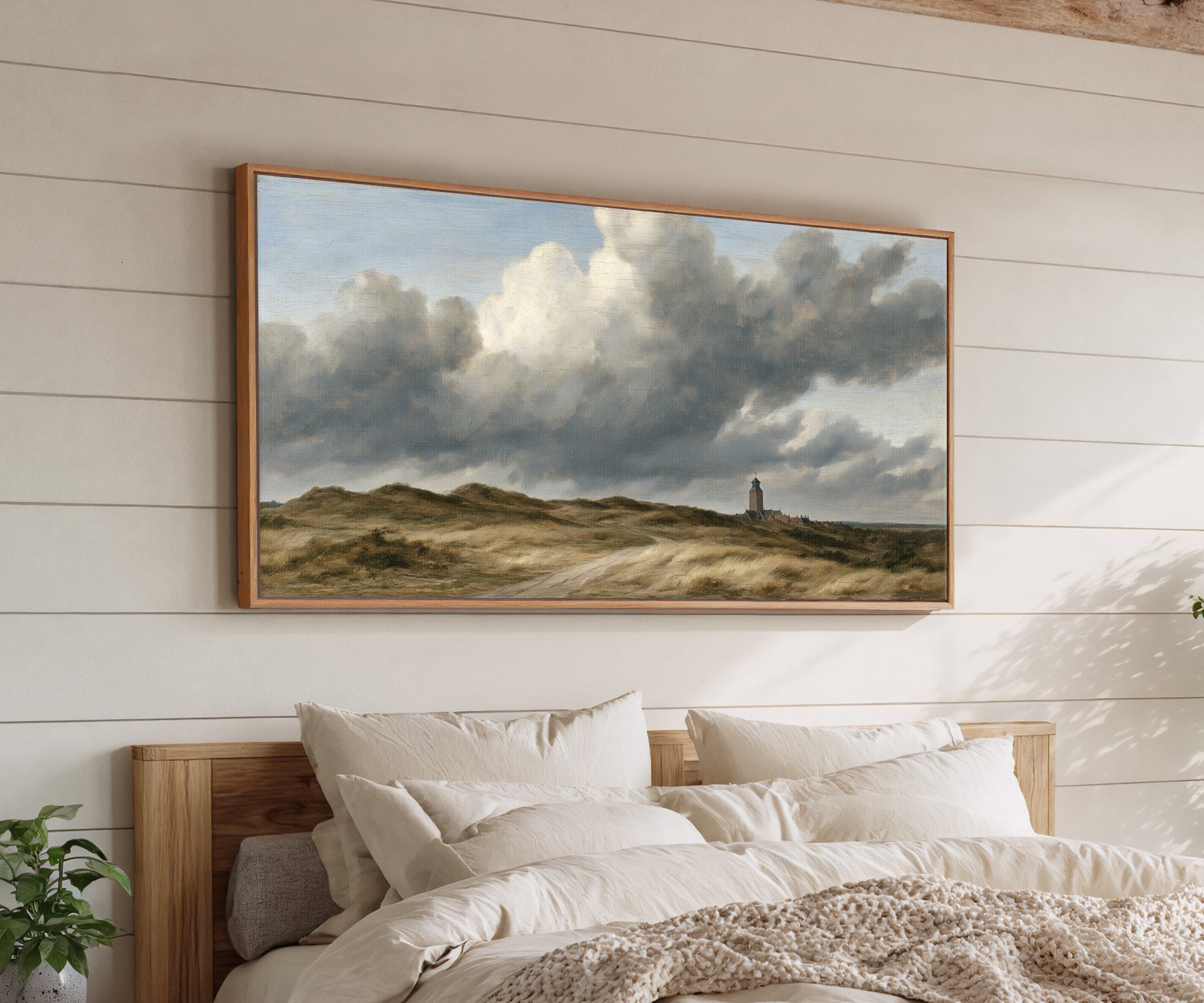 low dunes under towering wind driven clouds canvas wall art in an oak frame above a bed