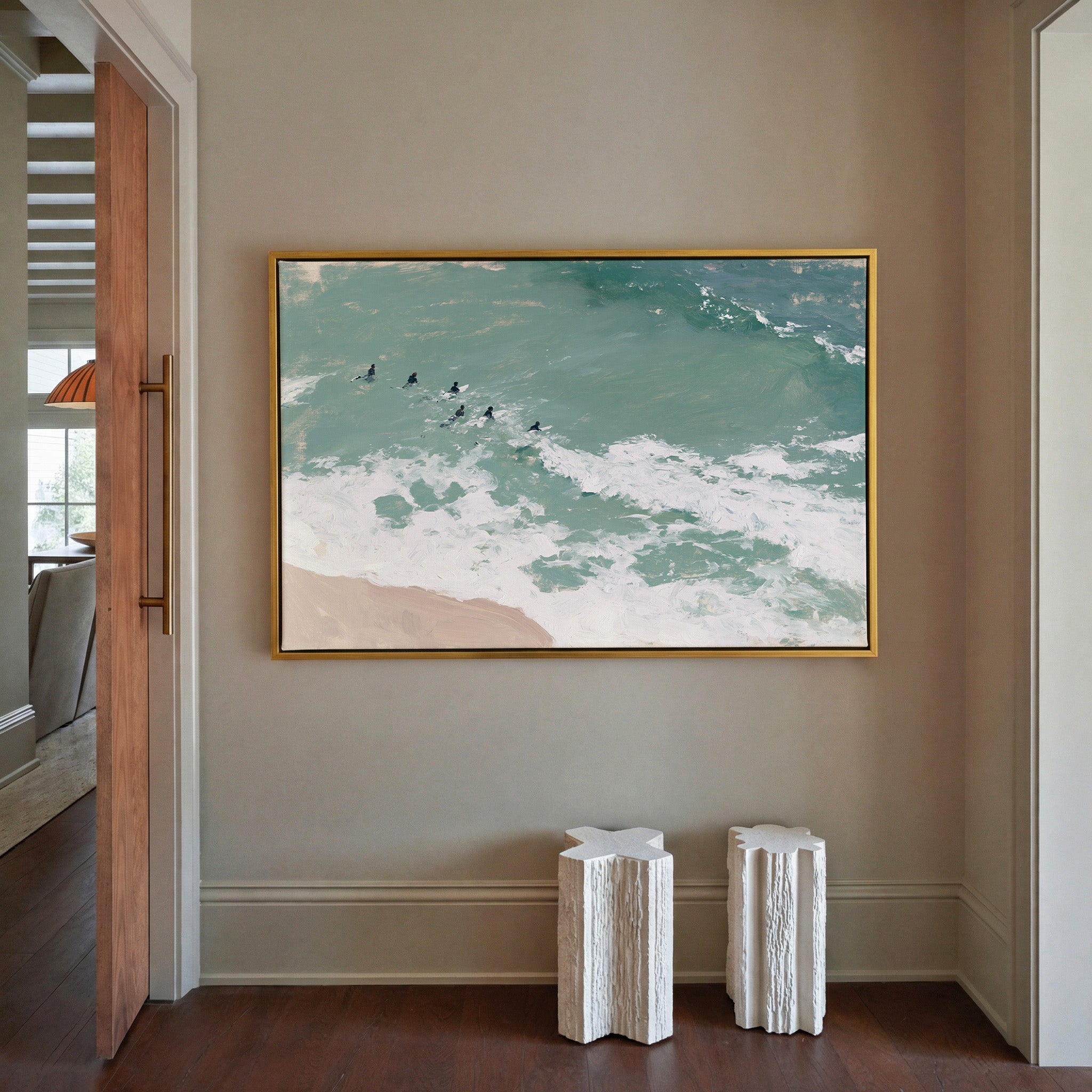 turquoise surf with small figures beyond the canvas wall art in a gold frame in a styled room setting