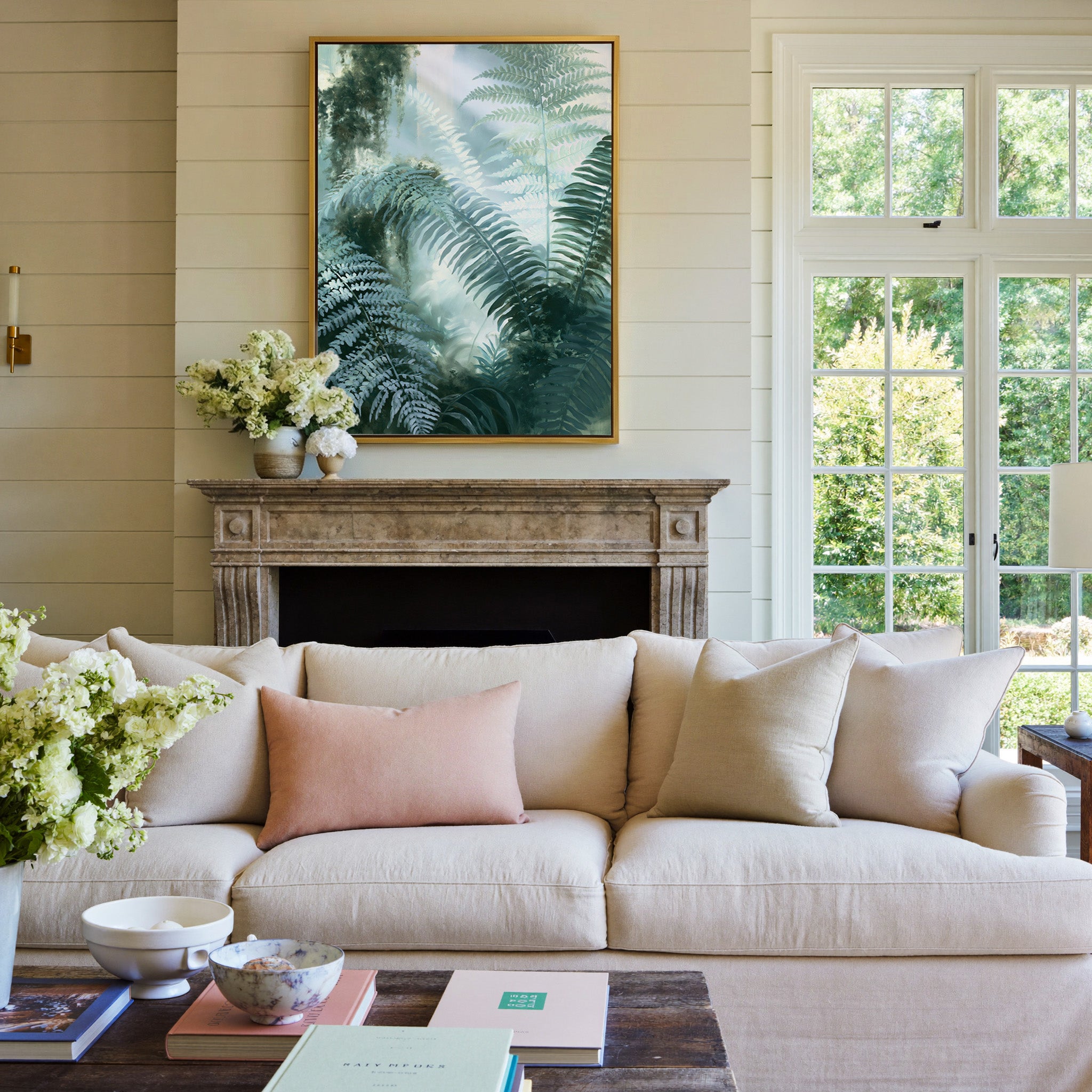 soft green fern fronds over a misted blue gray canvas wall art in a gold frame above a mantel