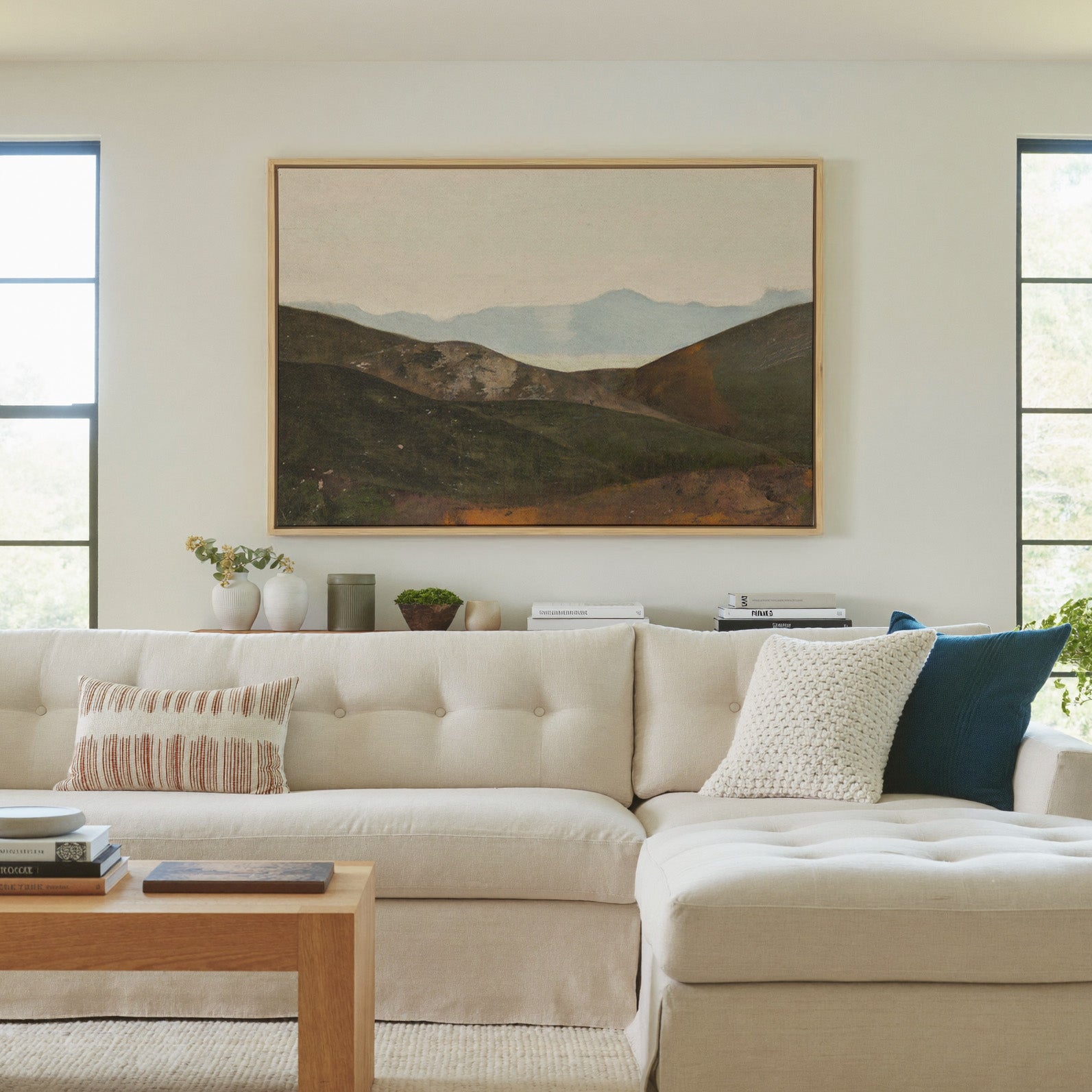 soft blue mountain landscape with dark canvas wall art in a natural wood frame in a living room