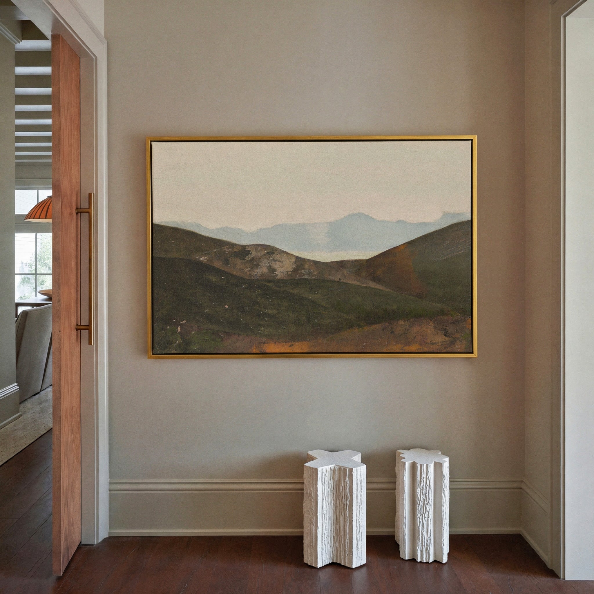 soft blue mountain landscape with dark canvas wall art in a gold frame in a styled room setting