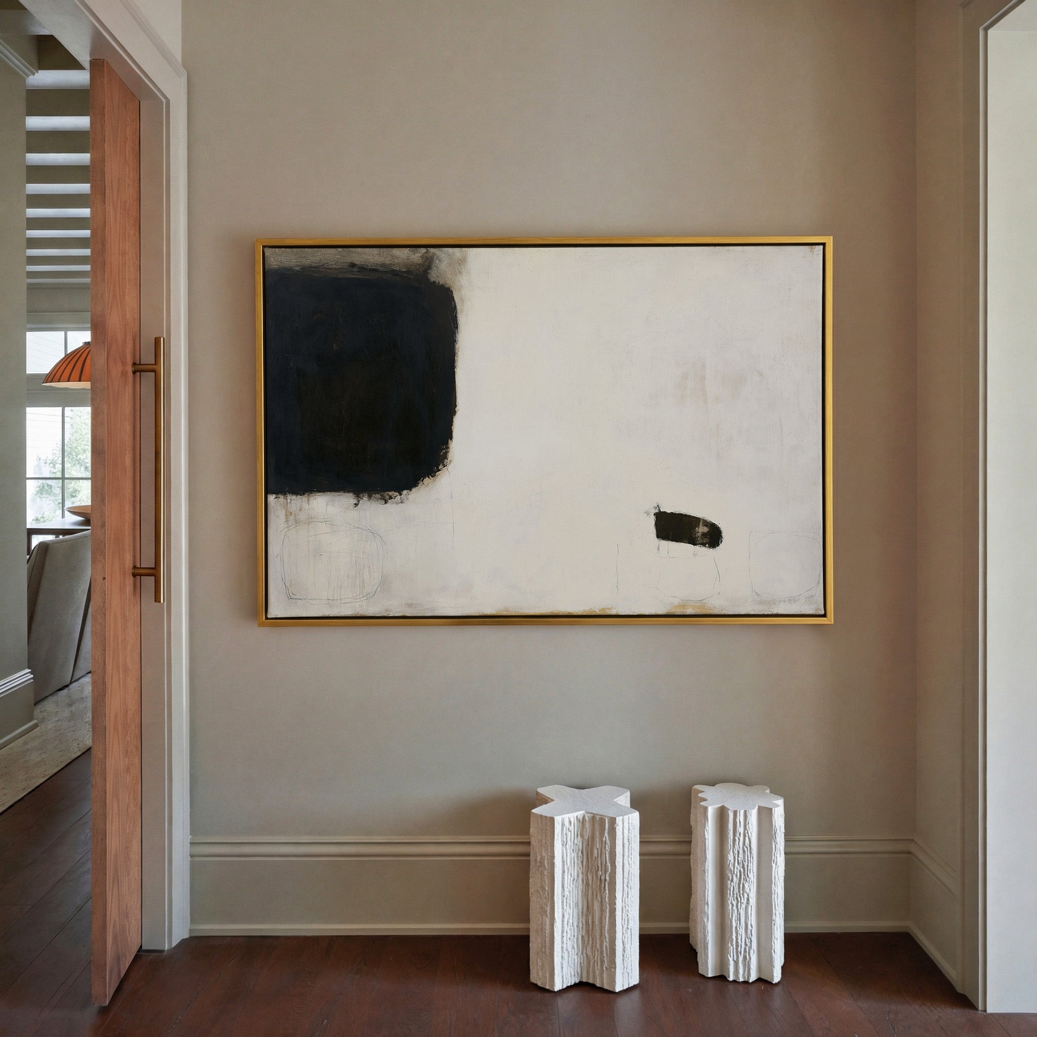 sparse black and cream abstract with heavy dark canvas wall art in a gold frame in a styled room setting