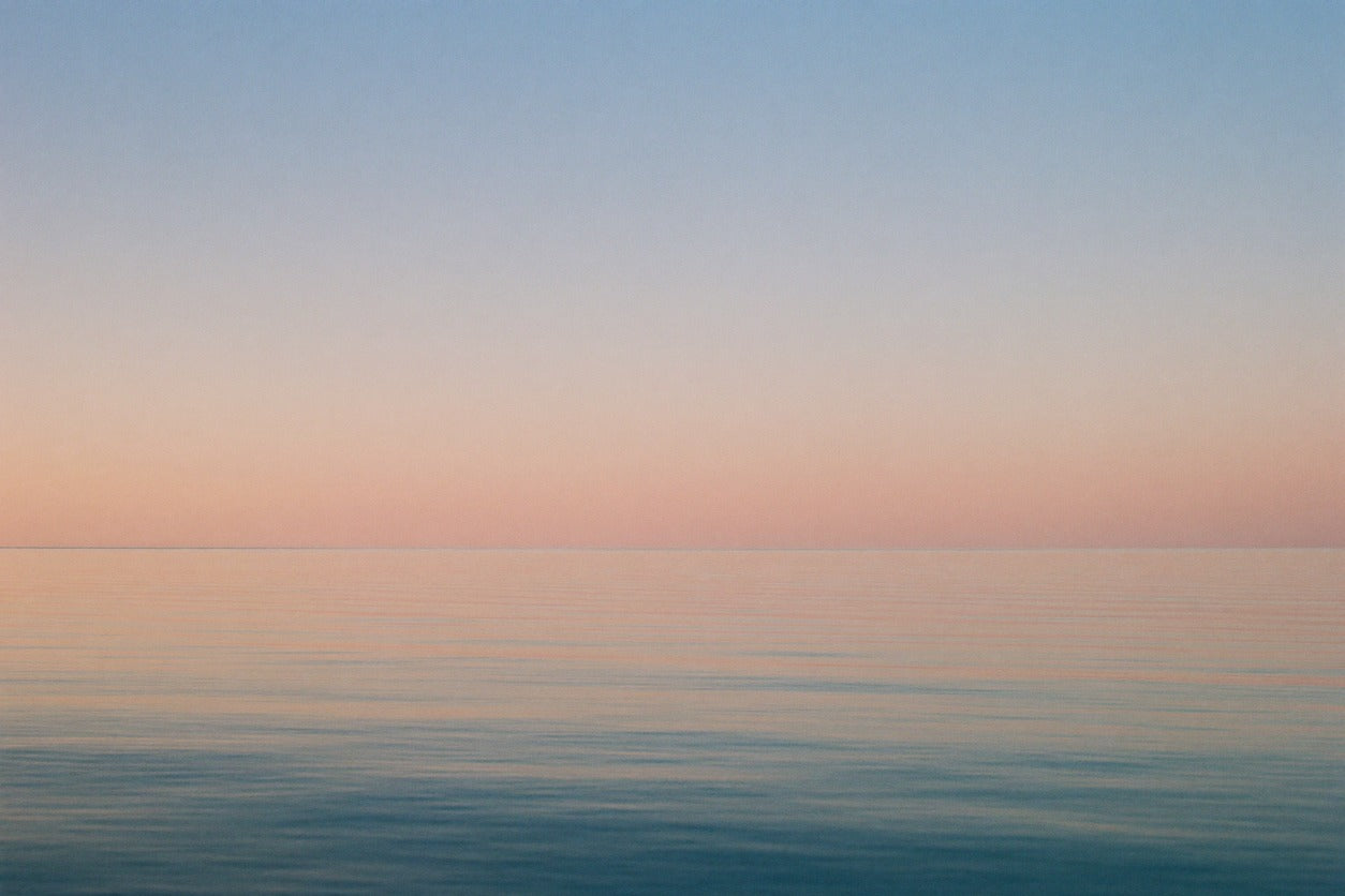 Pastel horizon over calm blue sea with peach sky and fine horizontal ripples