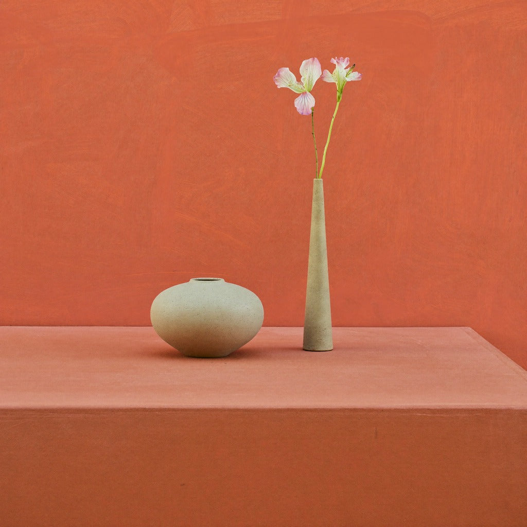 Rounded beige vessel and tall slim vase with pale blossoms against a terracotta wall