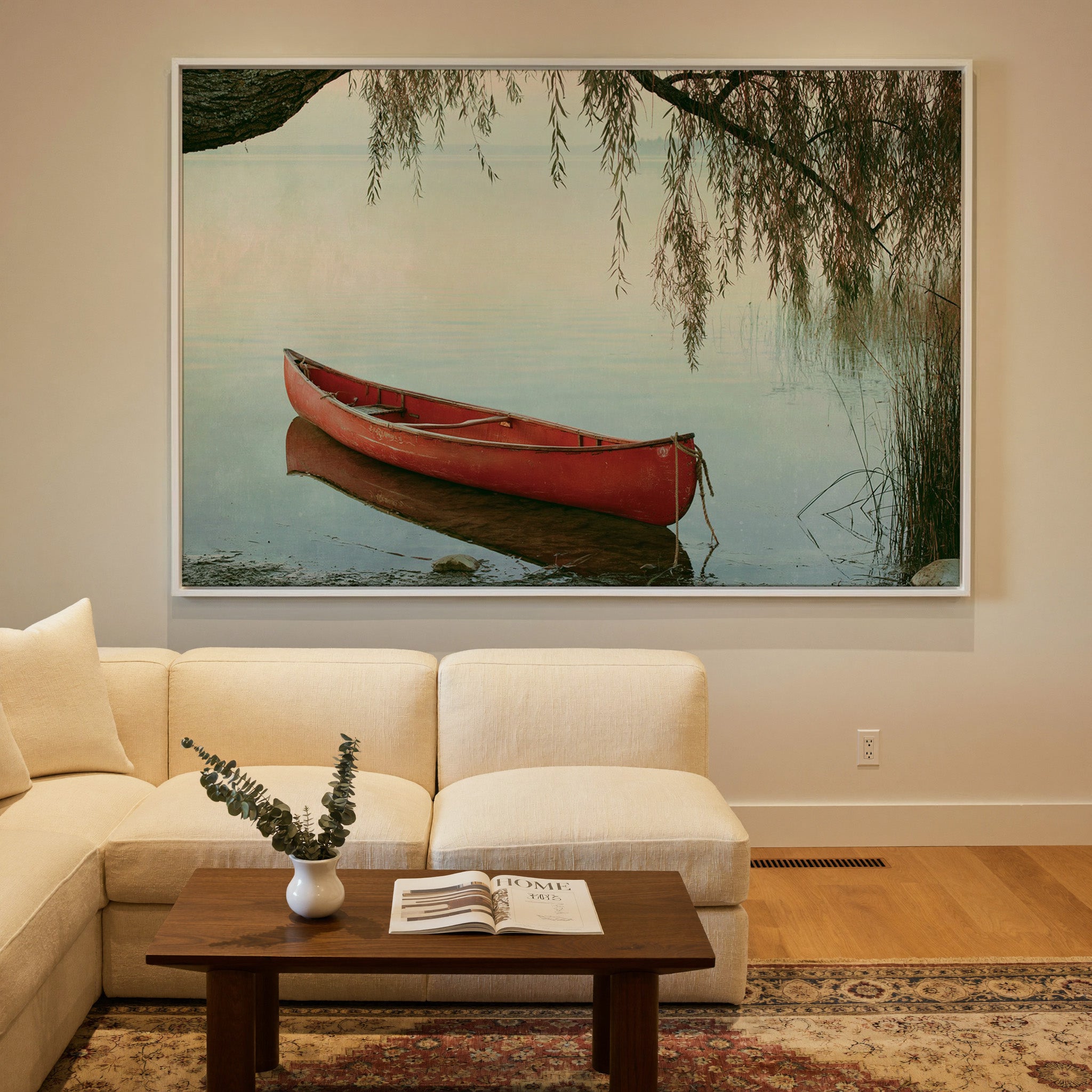 red canoe under hanging willow branches by canvas wall art in a white frame in a styled room setting