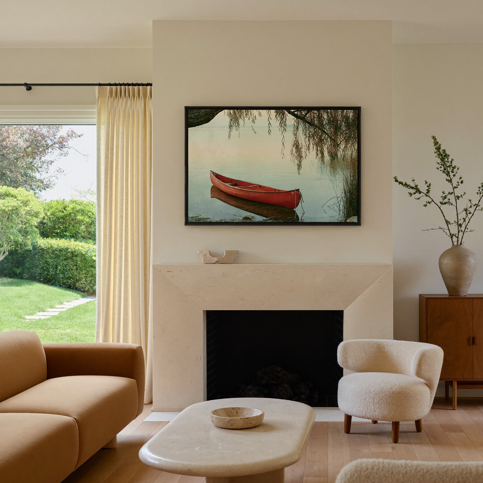 red canoe under hanging willow branches by canvas wall art in a black frame above a mantel