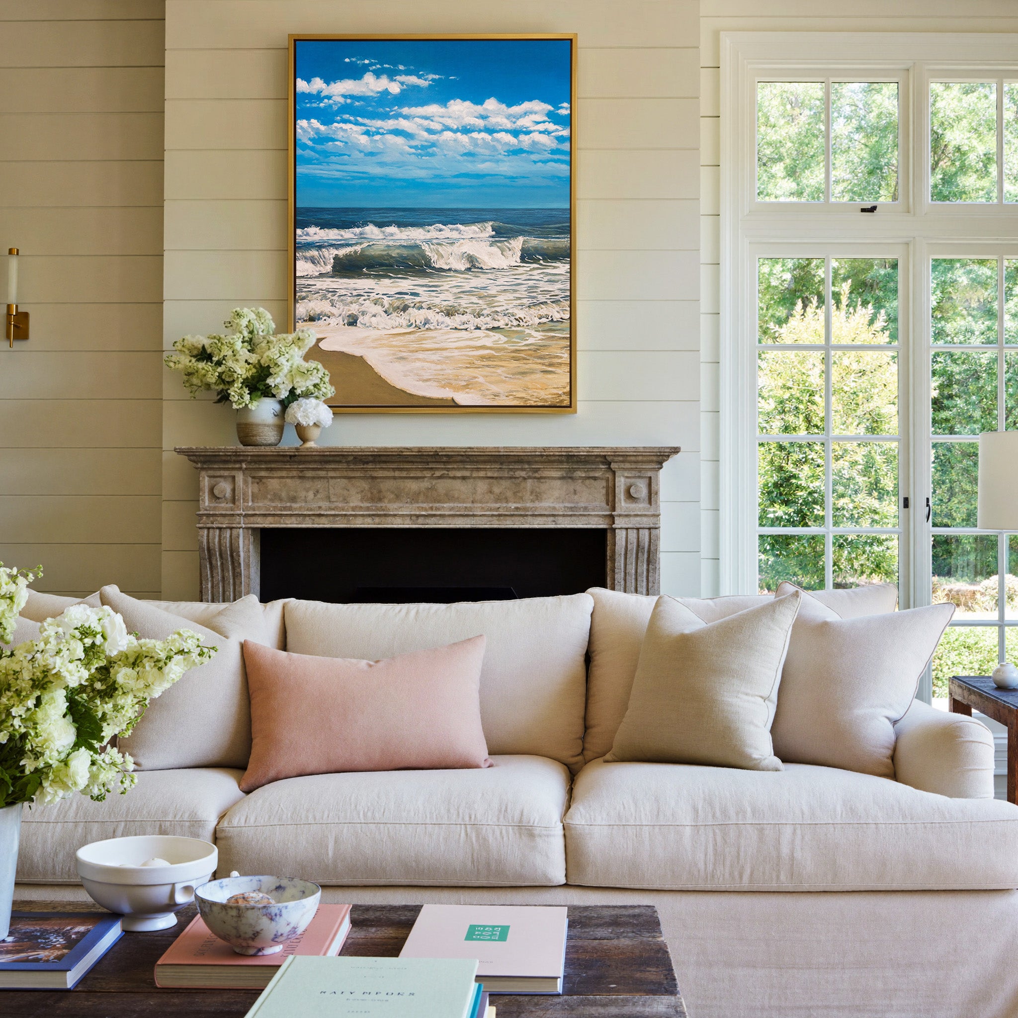 bright blue seascape with foamy surf and a wide canvas wall art in a gold frame above a mantel