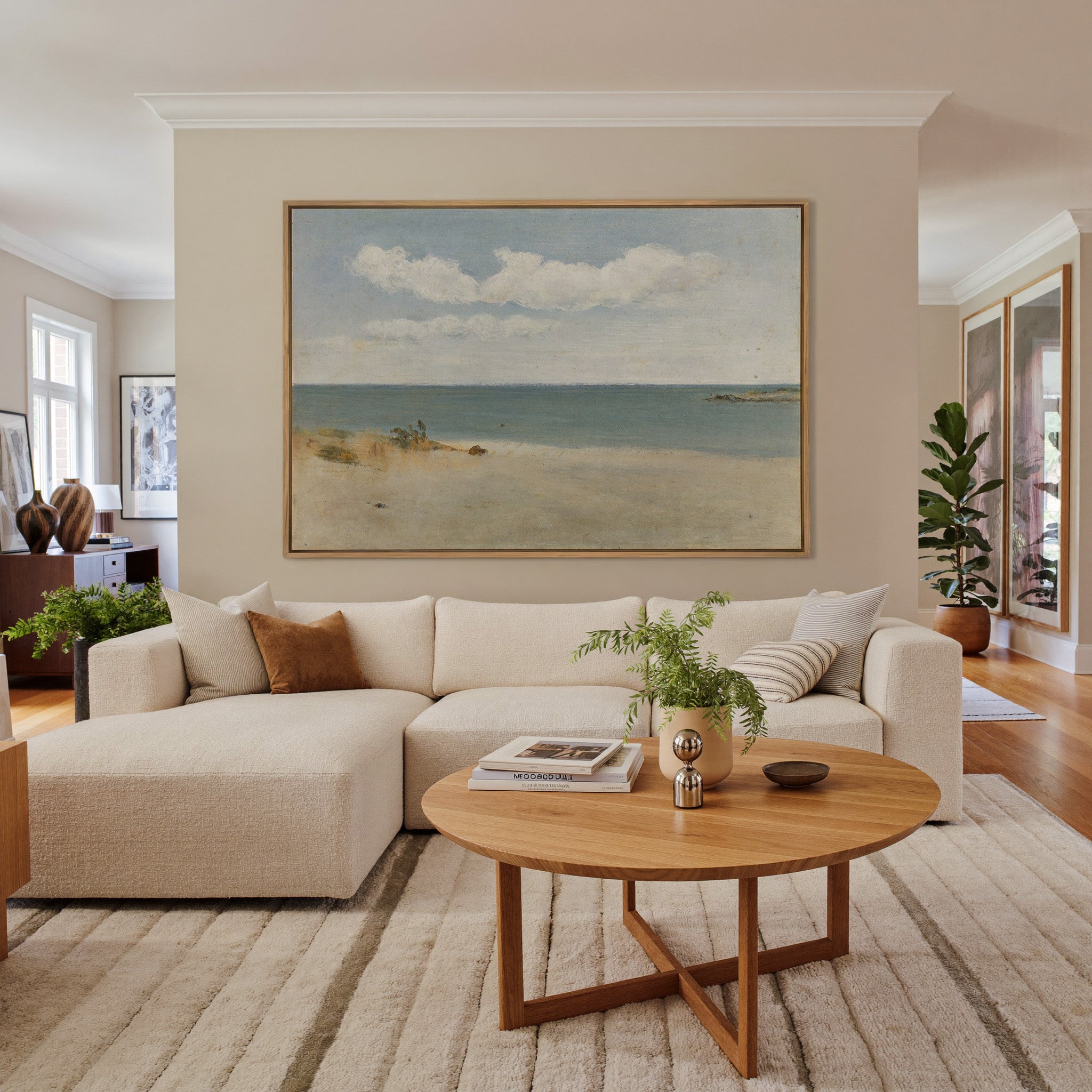 pale beach, blue green water, and broad white canvas wall art in an oak frame in a living room