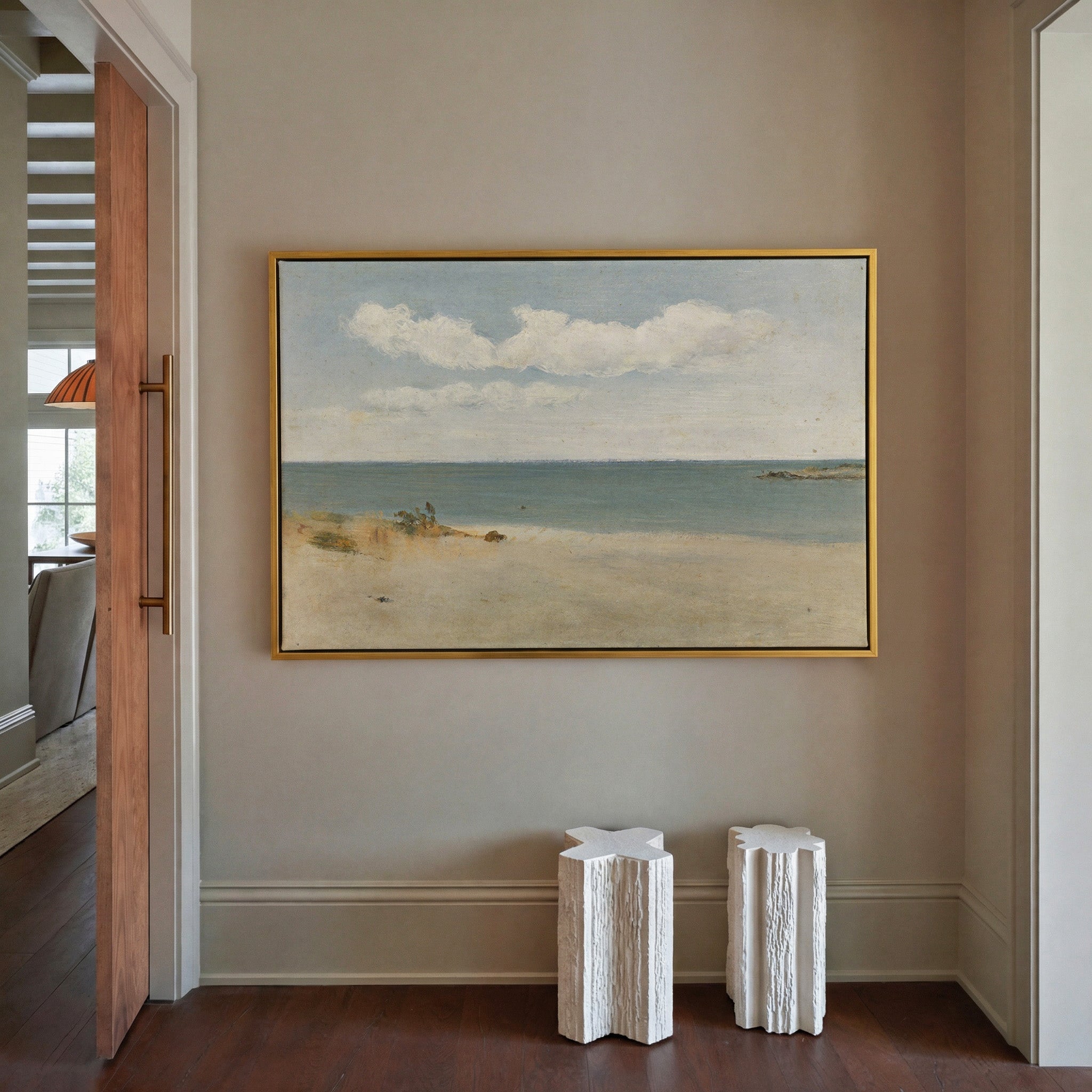 pale beach, blue green water, and broad white canvas wall art in a gold frame in a styled room setting