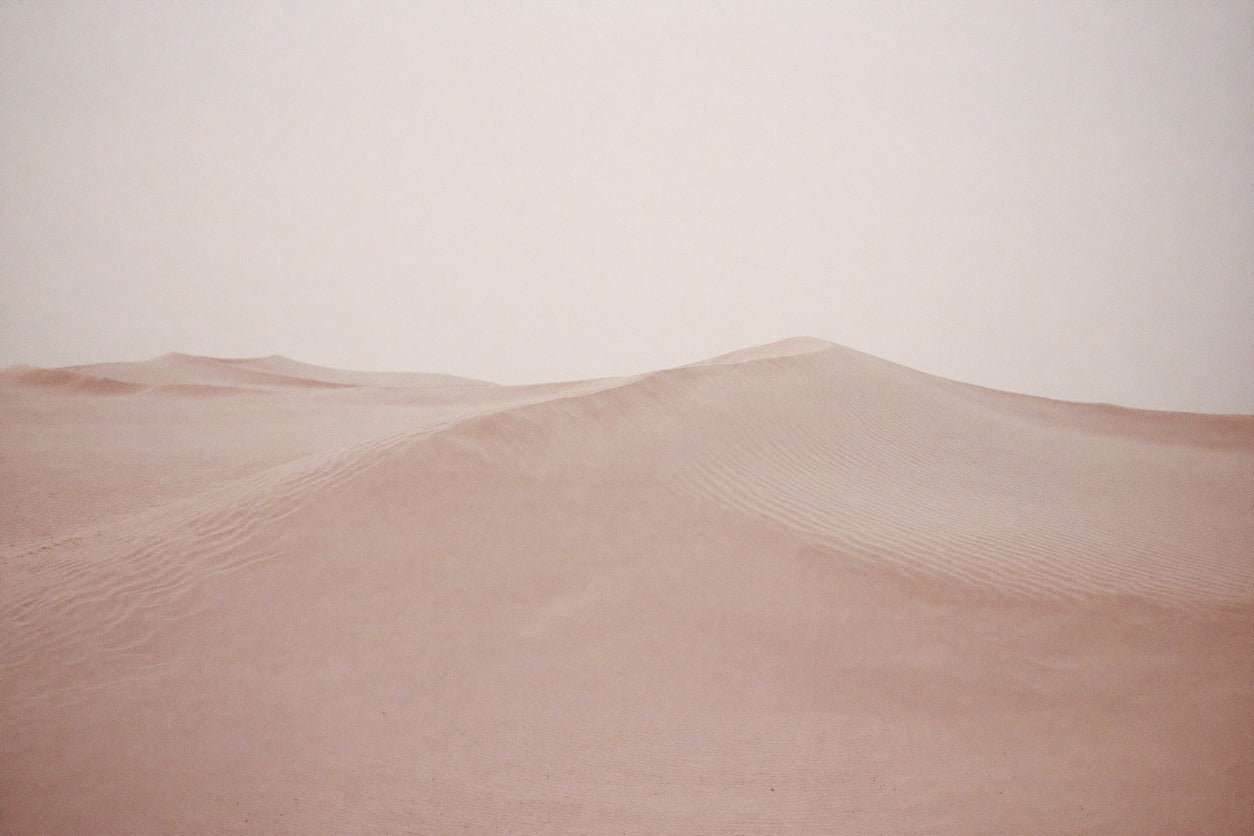 Soft blush desert dunes with rippled sand and a pale open sky across the frame