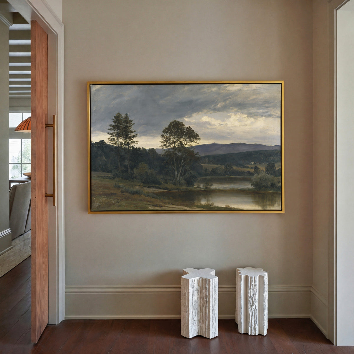 moody river landscape with trees and distant canvas wall art in a gold frame in a styled room setting