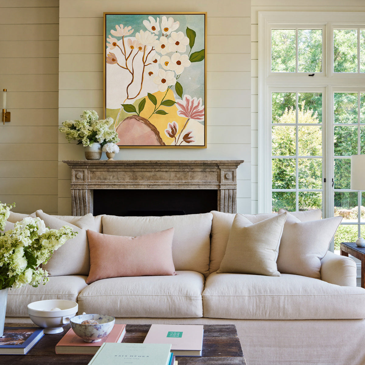 soft white blossoms with green leaves on a pale canvas wall art in a gold frame above a mantel