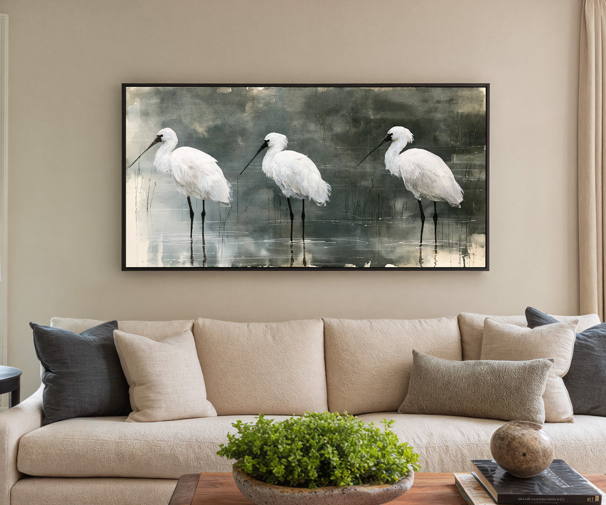 three white birds in shallow marsh water canvas wall art in a black frame in a styled room setting