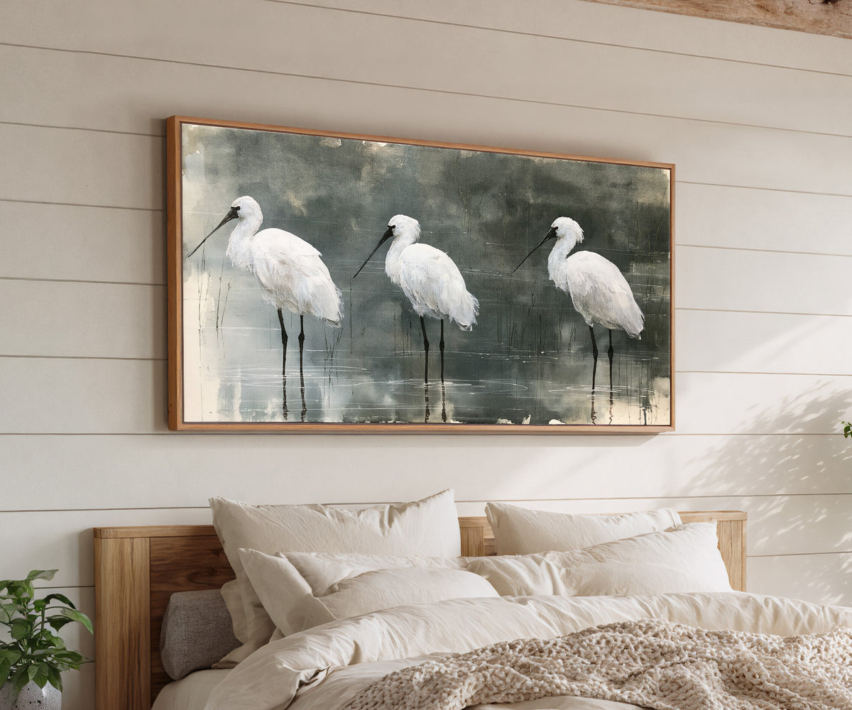 three white birds in shallow marsh water canvas wall art in an oak frame above a bed