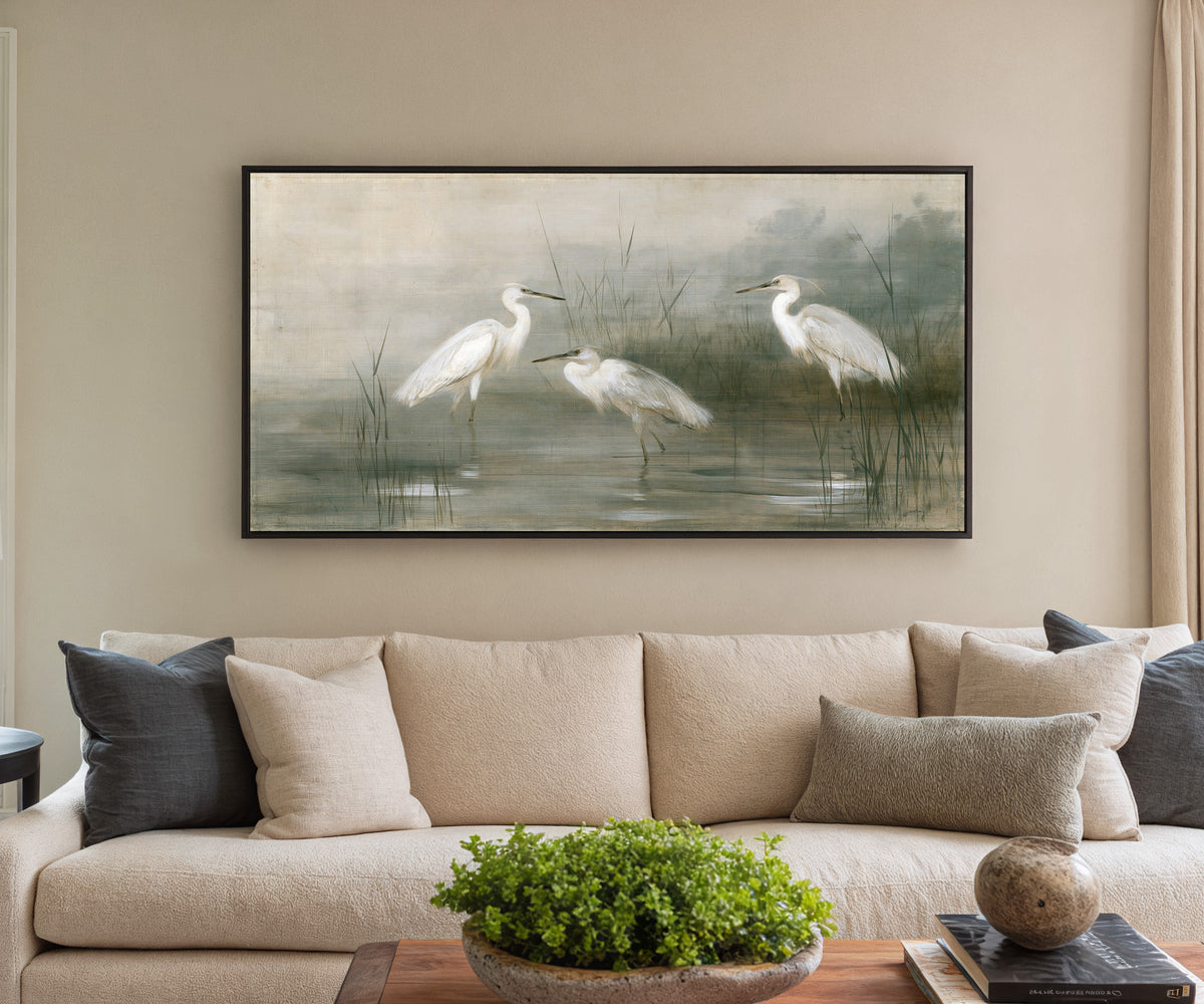 three white birds in shallow marsh water canvas wall art in a black frame in a styled room setting