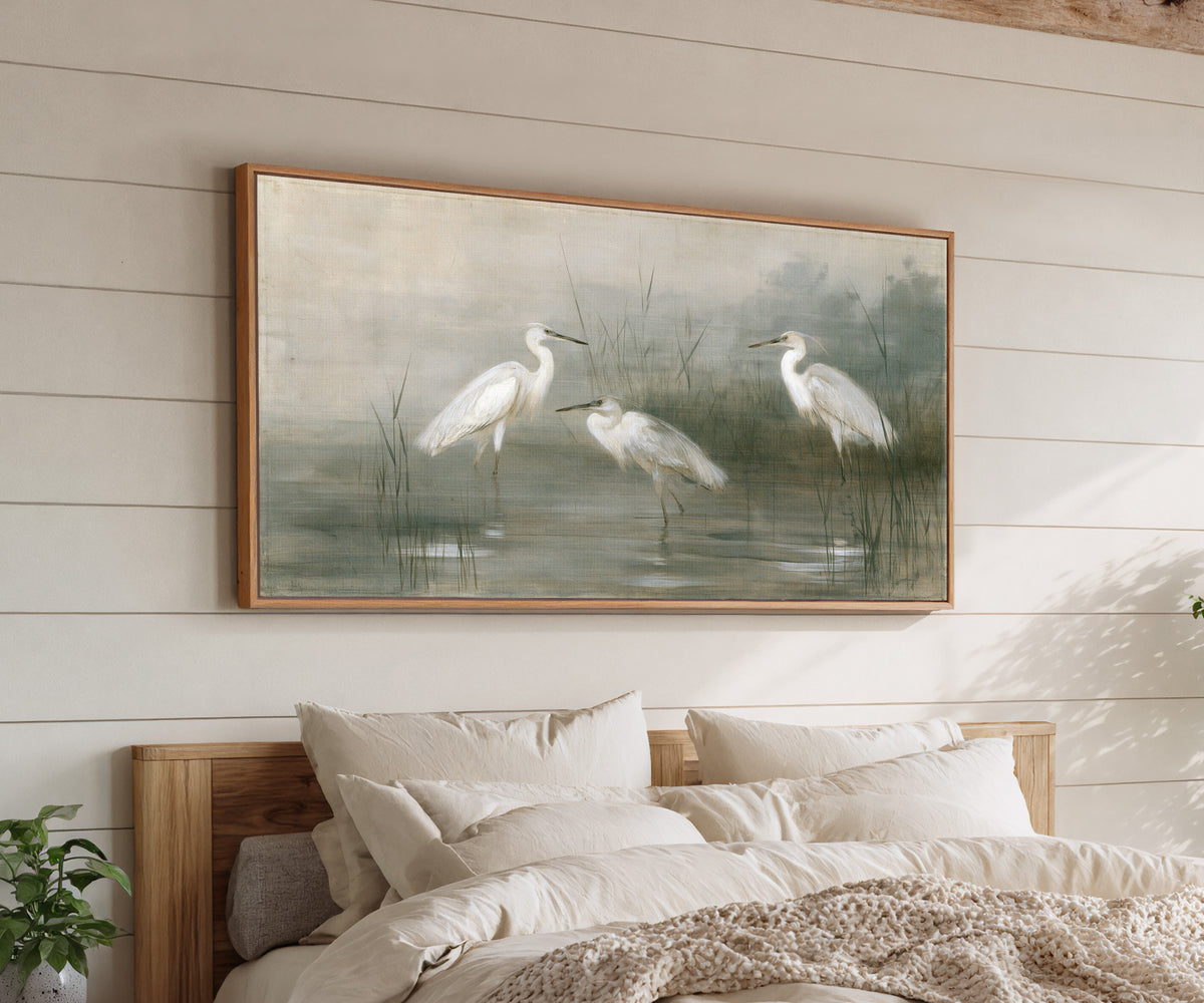 three white birds in shallow marsh water canvas wall art in an oak frame above a bed