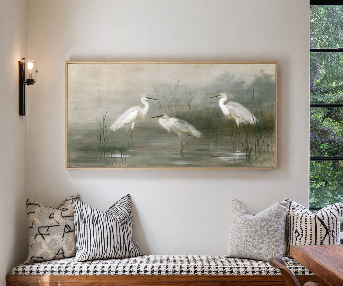 three white birds in shallow marsh water canvas wall art in a natural wood frame in a living room