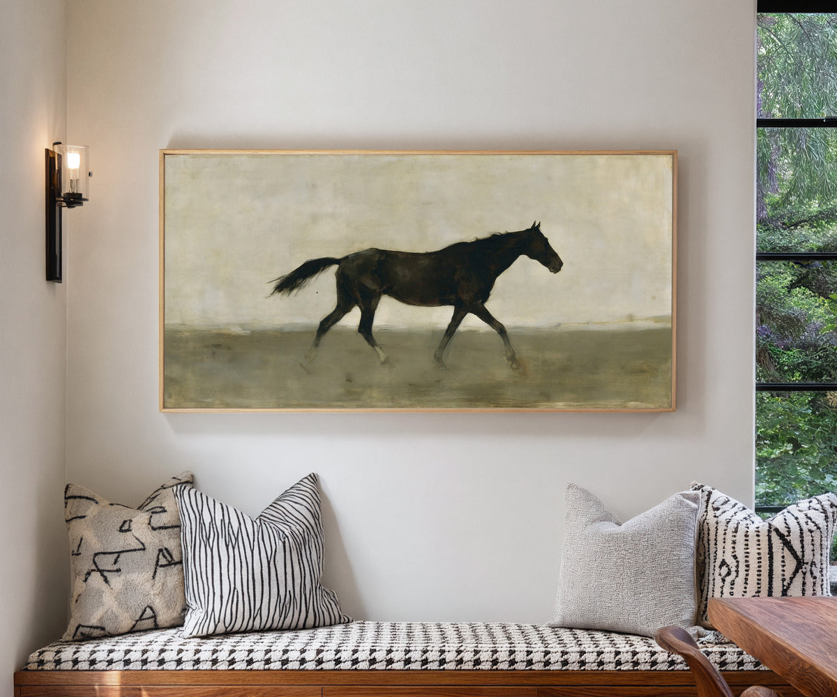 single dark horse in a pale open field canvas wall art in a natural wood frame in a living room