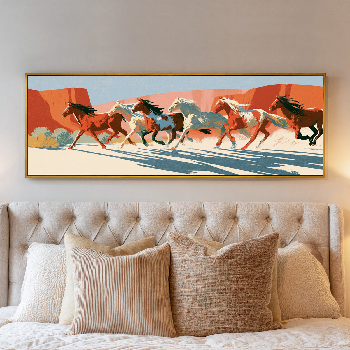 running horse herd beneath terracotta cliffs canvas wall art in a gold floater frame above a bed