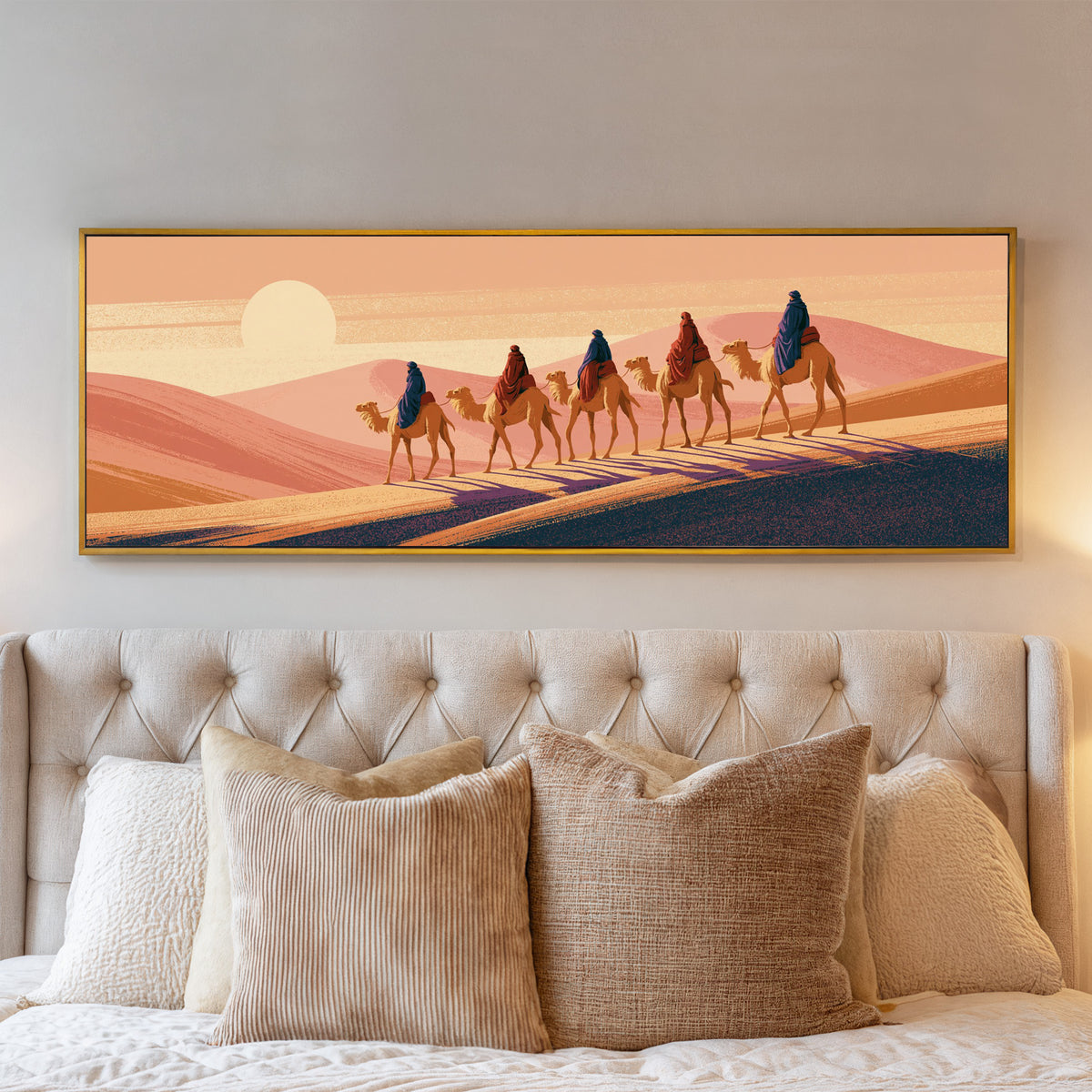 five camel riders crossing peach dunes beneath canvas wall art in a gold floater frame above a bed