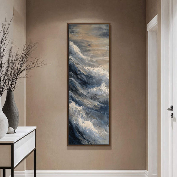 This vertical canvas print features an abstract expressionist painting of churning ocean waves in a palette of deep blues, grays, and whites, set against a warm taupe wall above a.