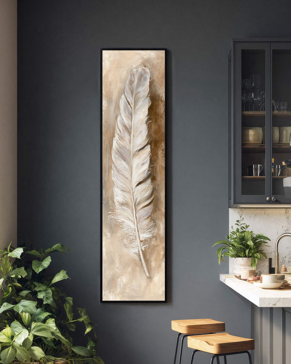 This vertical canvas wall art features a painterly white feather in a neutral palette, displayed in a black floater frame on a charcoal kitchen wall beside a cabinet.