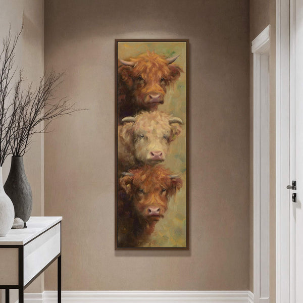 This vertical, impressionistic canvas wall art features three Highland cows stacked vertically against a textured, tan wall, complementing a console table with a vase and branches.