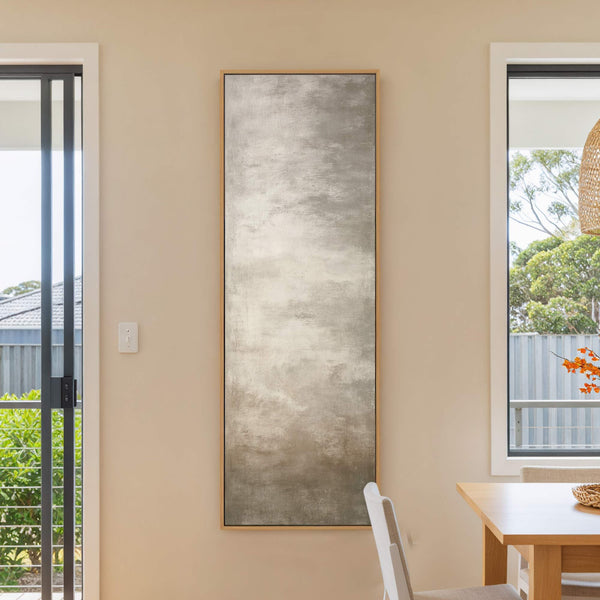 This vertical canvas wall art features an abstract subject with a neutral gray and white palette in a painterly style, hanging on a beige wall next to a window and.