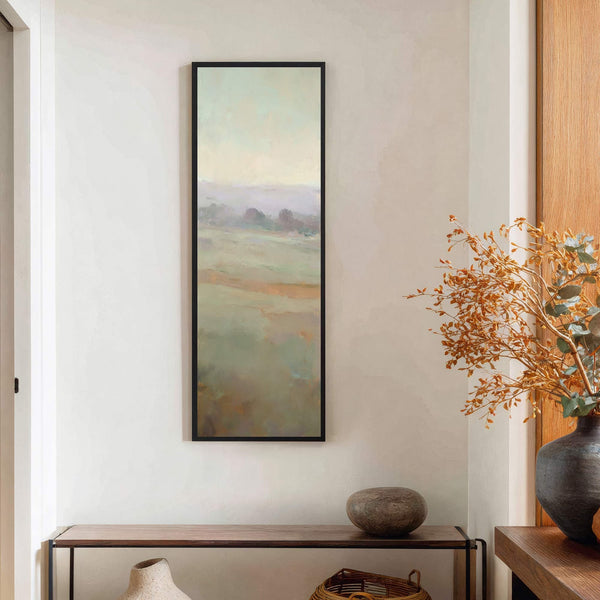 A vertical, abstract landscape painting print with a soft palette of greens, yellows, and purples is displayed on a textured white wall above a console table.