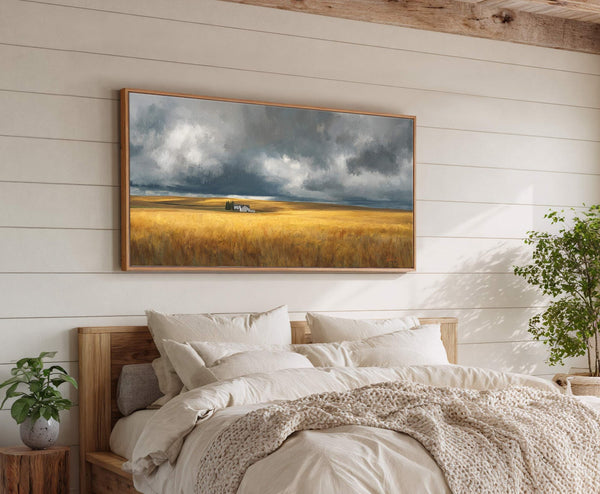 This horizontal canvas wall art displays a dramatic landscape with a golden field under a dark, cloudy sky with a white farmhouse. The artwork is framed in natural wood and.