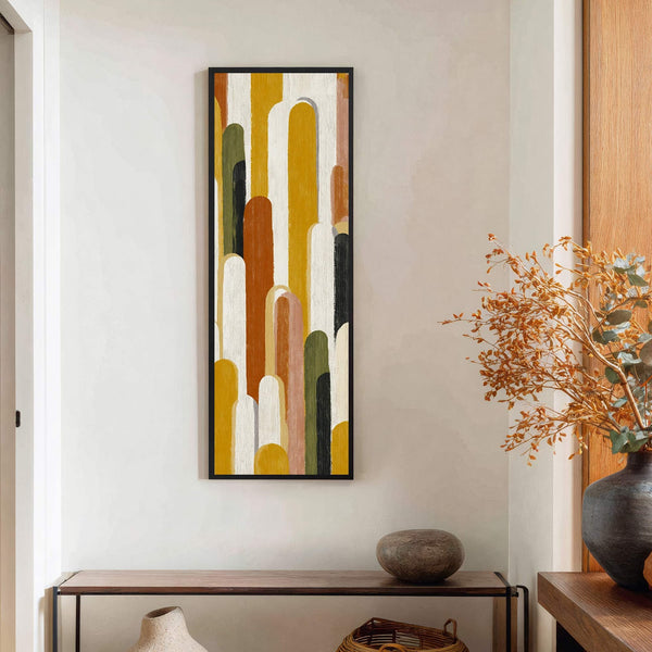 This vertical canvas wall art features an abstract design with rounded shapes in a warm, earthy palette of yellow, rust, and green, framed in black and displayed above a wooden.