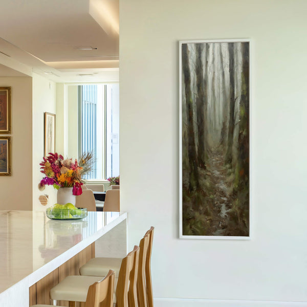 This vertical, impressionistic art print features a misty forest path rendered in earthy greens and browns. It is framed in white and hangs on a light-colored wall in a modern.