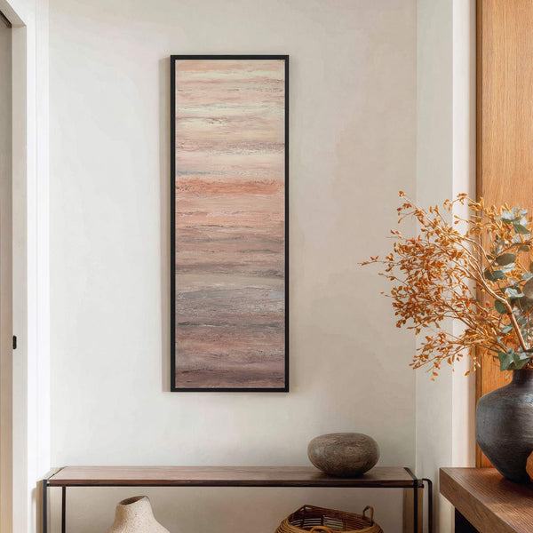 This vertical, rectangular canvas print features abstract brushstrokes in a muted palette of blush, cream, and gray. It is framed in black and hangs on a textured white wall above.