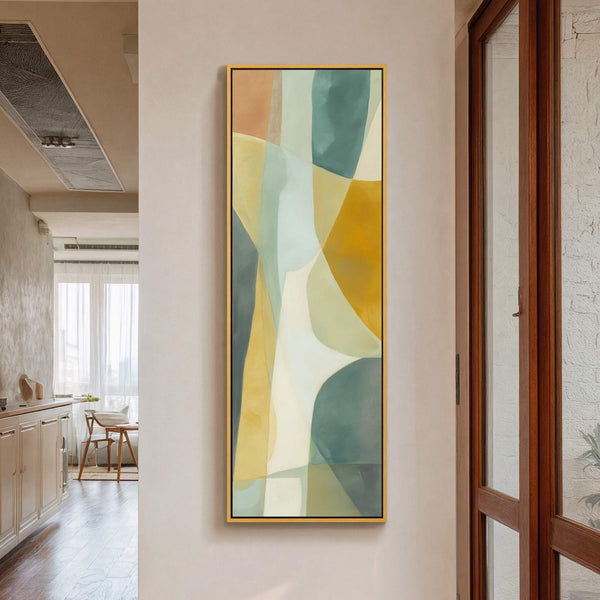 This vertical, abstract canvas wall art features a soft palette of earthy tones and muted greens within a thin gold floater frame, hanging on a light-colored wall with a wooden.