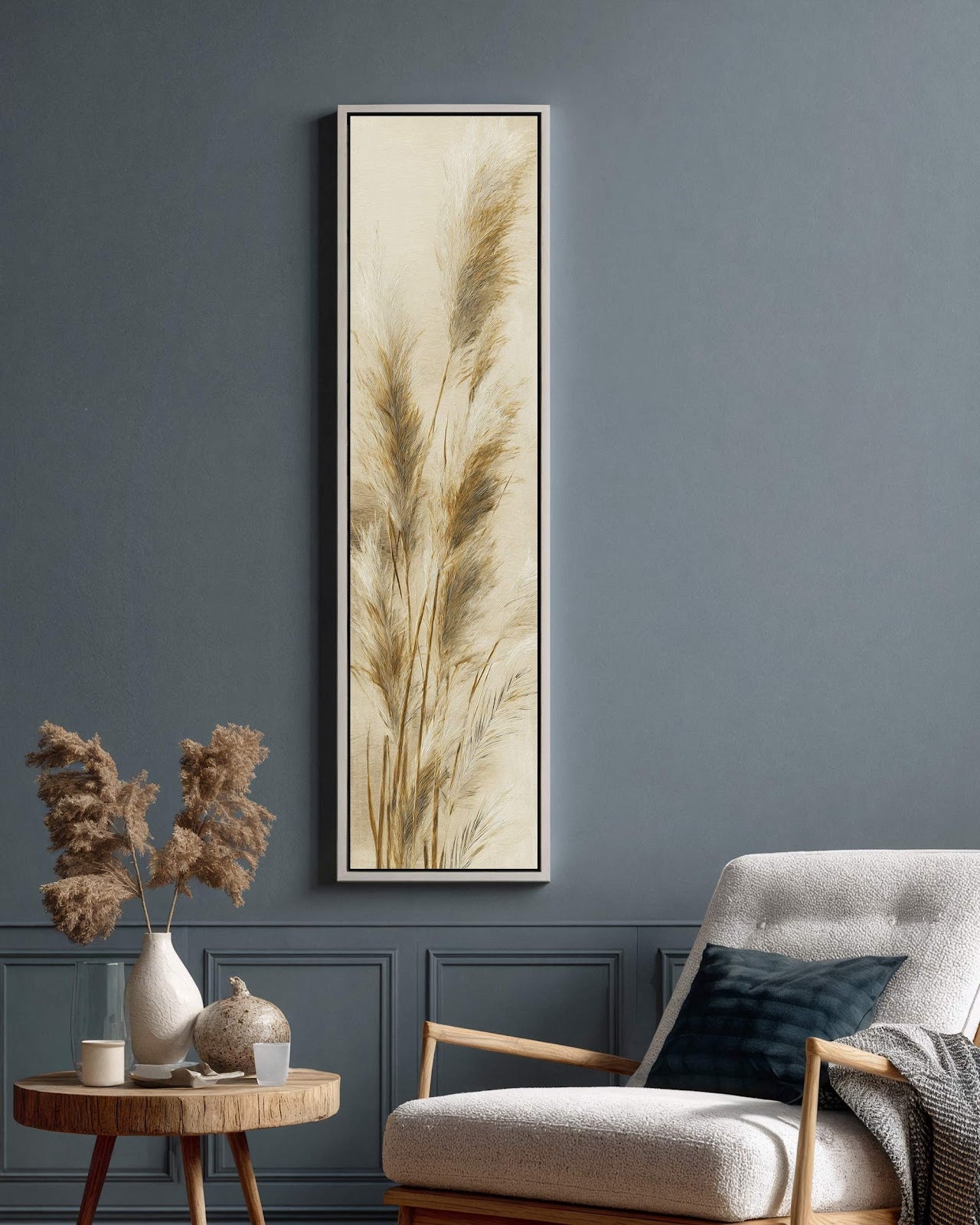 This vertical botanical canvas print features pampas grass in a beige palette, showcased in a white floater frame on a blue living room wall beside a white armchair.