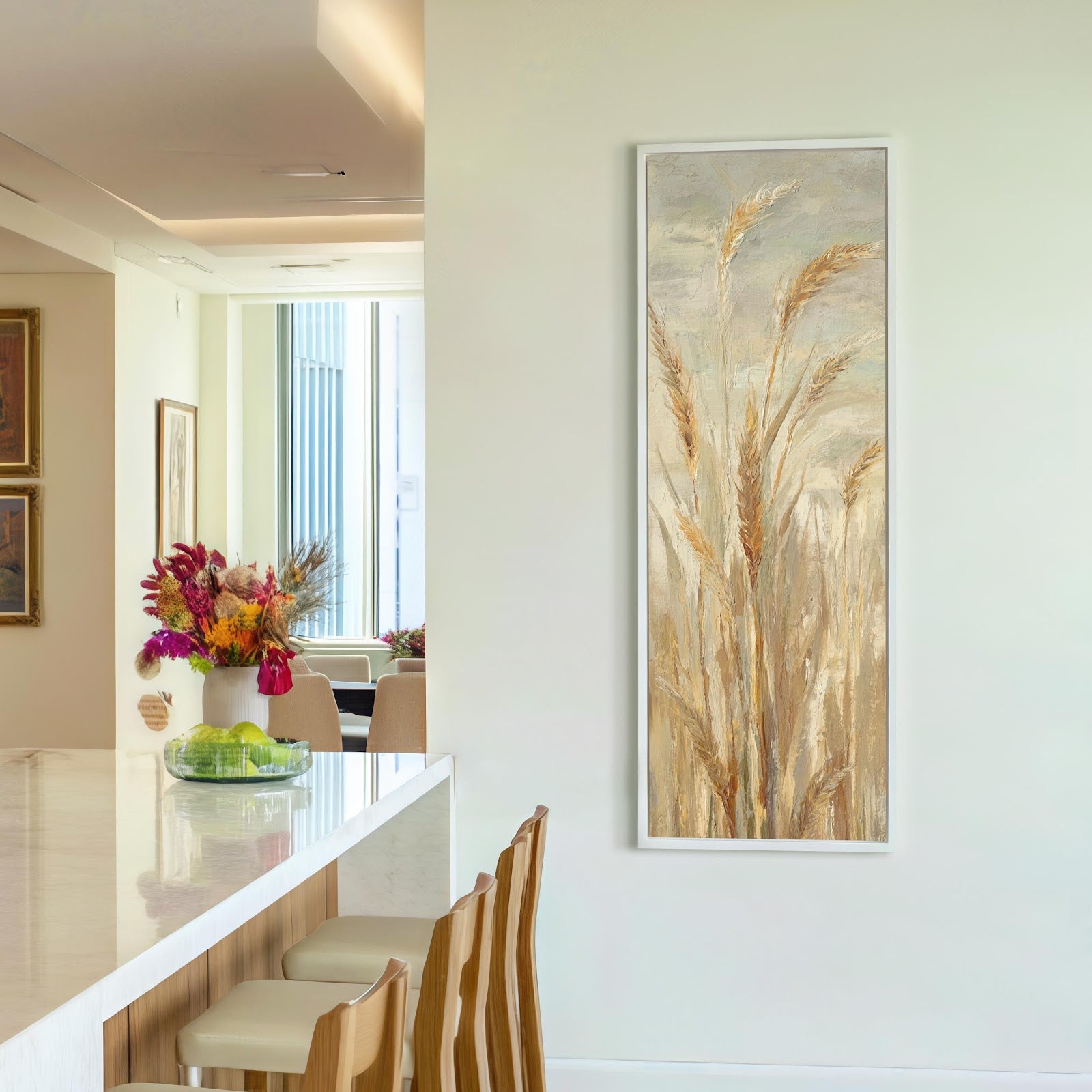 This vertical canvas art print features impressionistic wheat stalks in a warm neutral palette, showcased in a white floater frame on a cream wall beside a kitchen island.