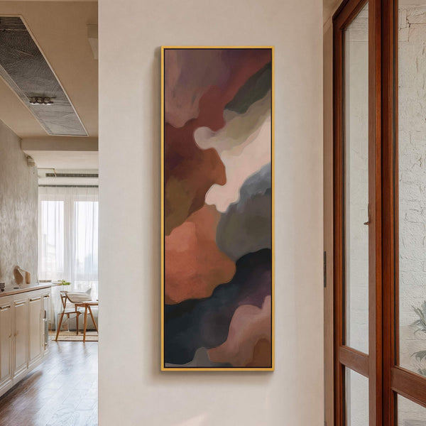 This vertical canvas wall art features an abstract design with a warm palette of rust, brown, and gray hues, framed in gold and displayed on a textured cream wall next.