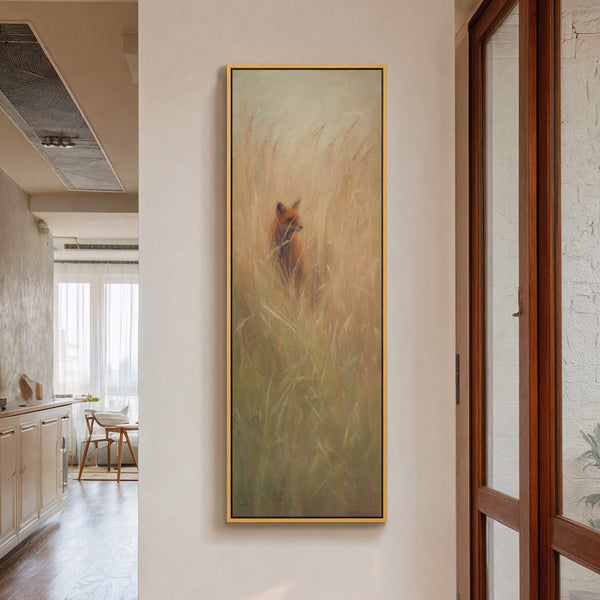 This vertical, painterly art print features a fox peeking through tall, golden grasses in a warm, earthy palette, framed in gold and displayed on a neutral wall.
