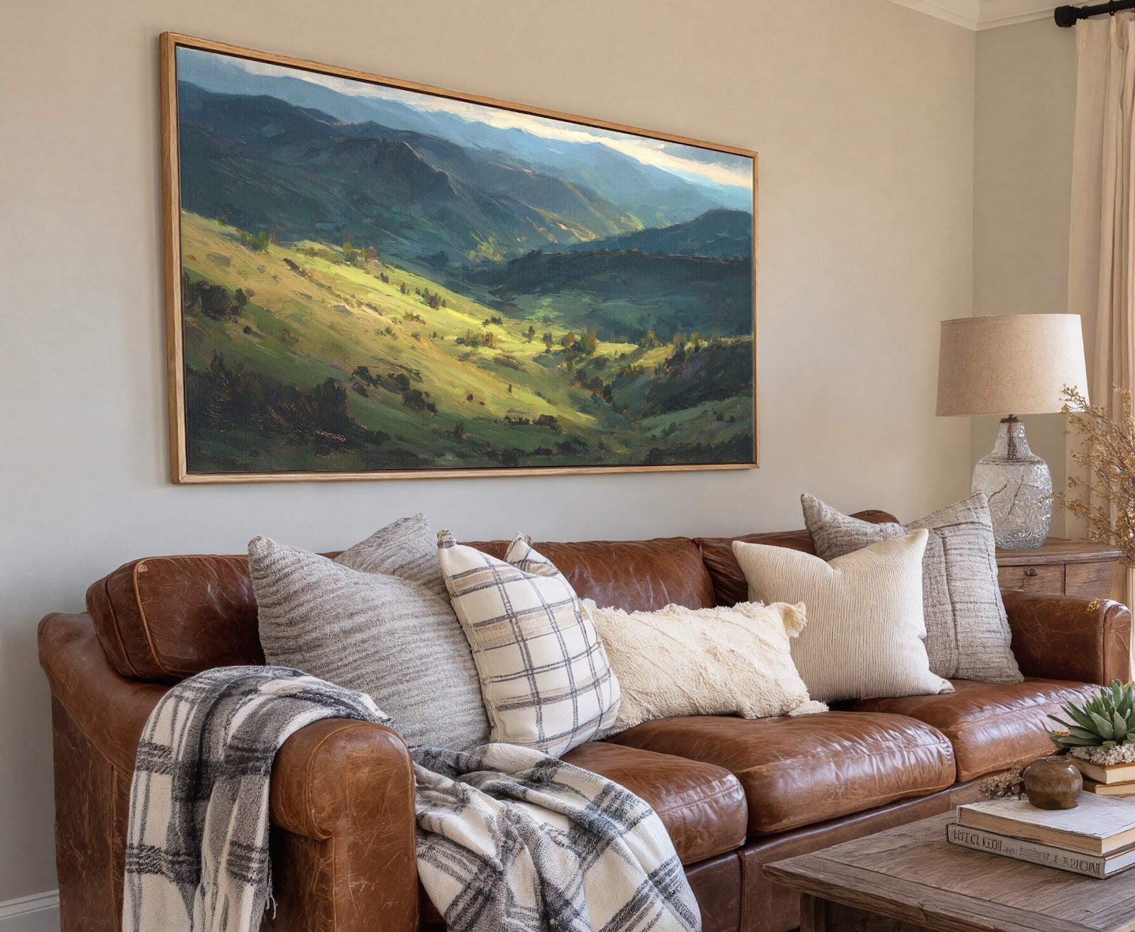 This horizontal landscape painting print features a green and blue palette and is framed in natural wood, hanging above a brown leather sofa on a light gray wall in a.